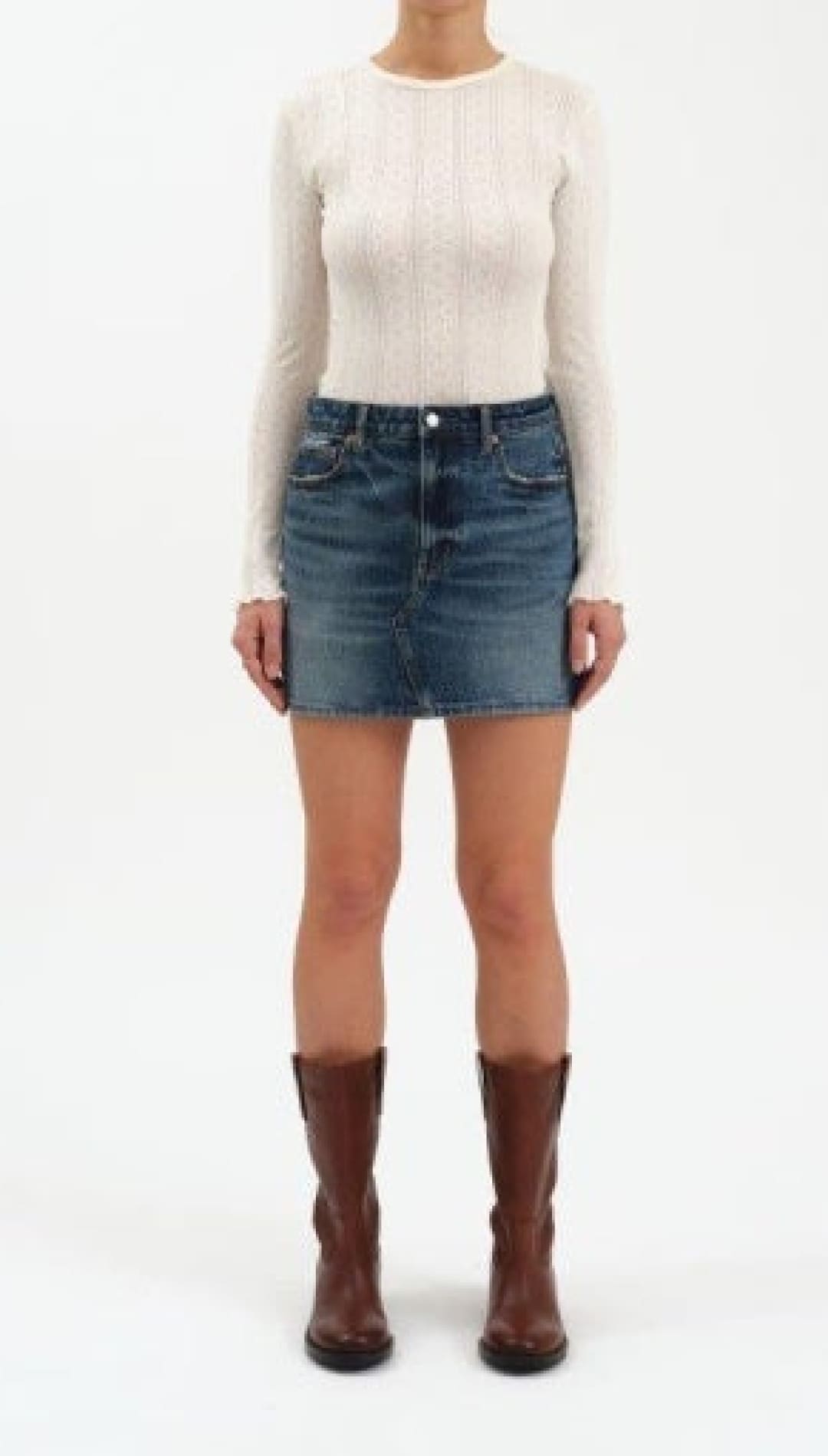 A woman wearing a long-sleeved white top, a blue denim mini-skirt, and brown knee-high boots.
