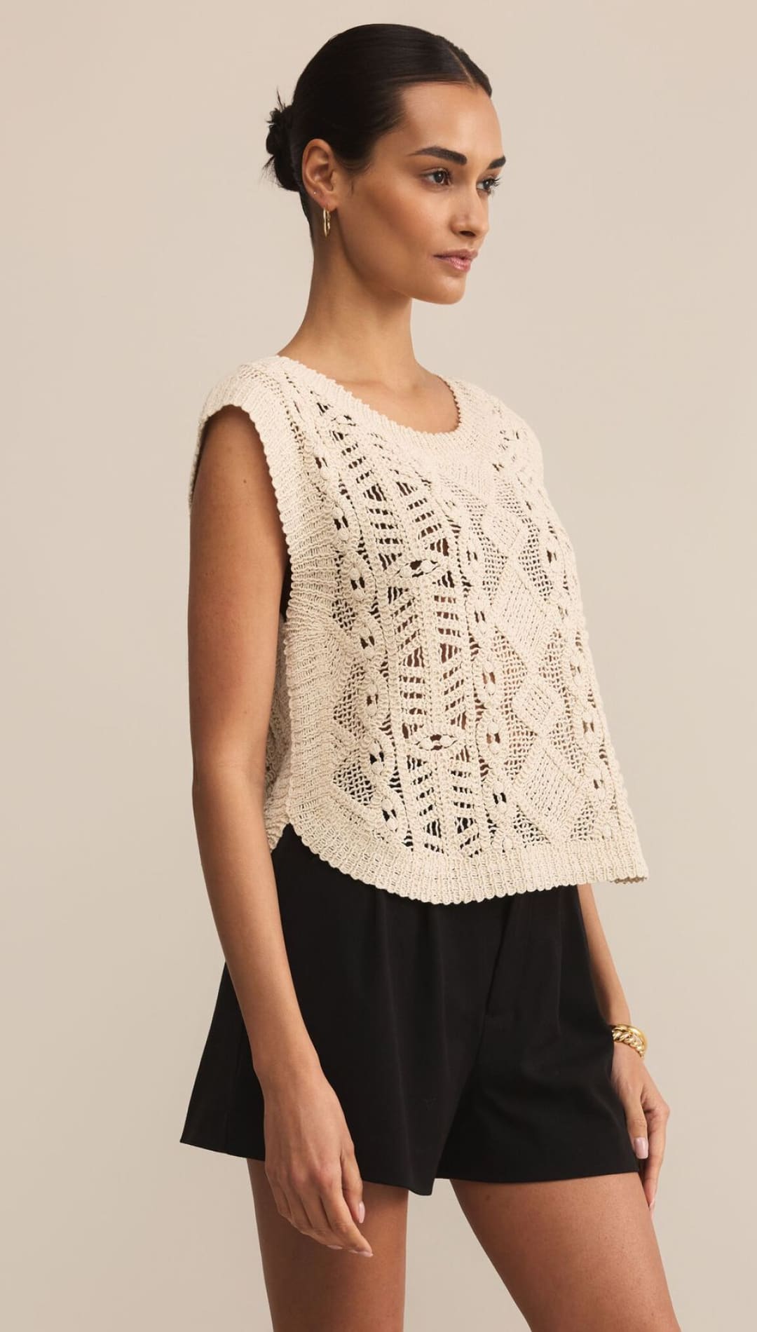 Women’s cream-colored crochet knit sleeveless top with black shorts.