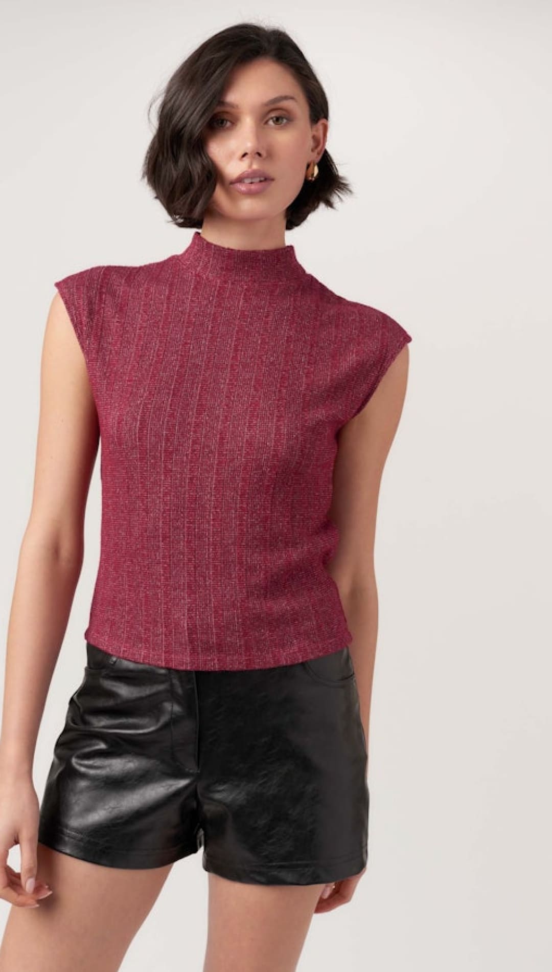 A woman in a short-sleeved maroon mock neck top and black leather shorts.