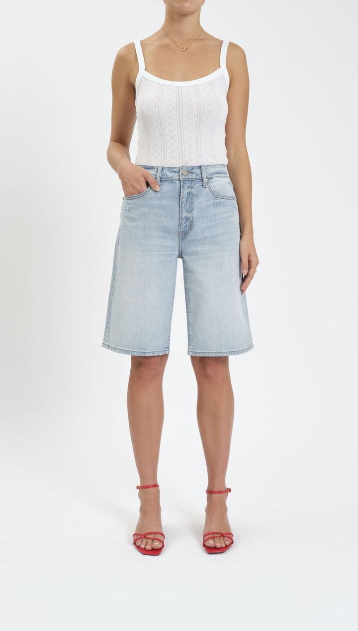 Woman wearing a white tank top and light blue denim shorts.