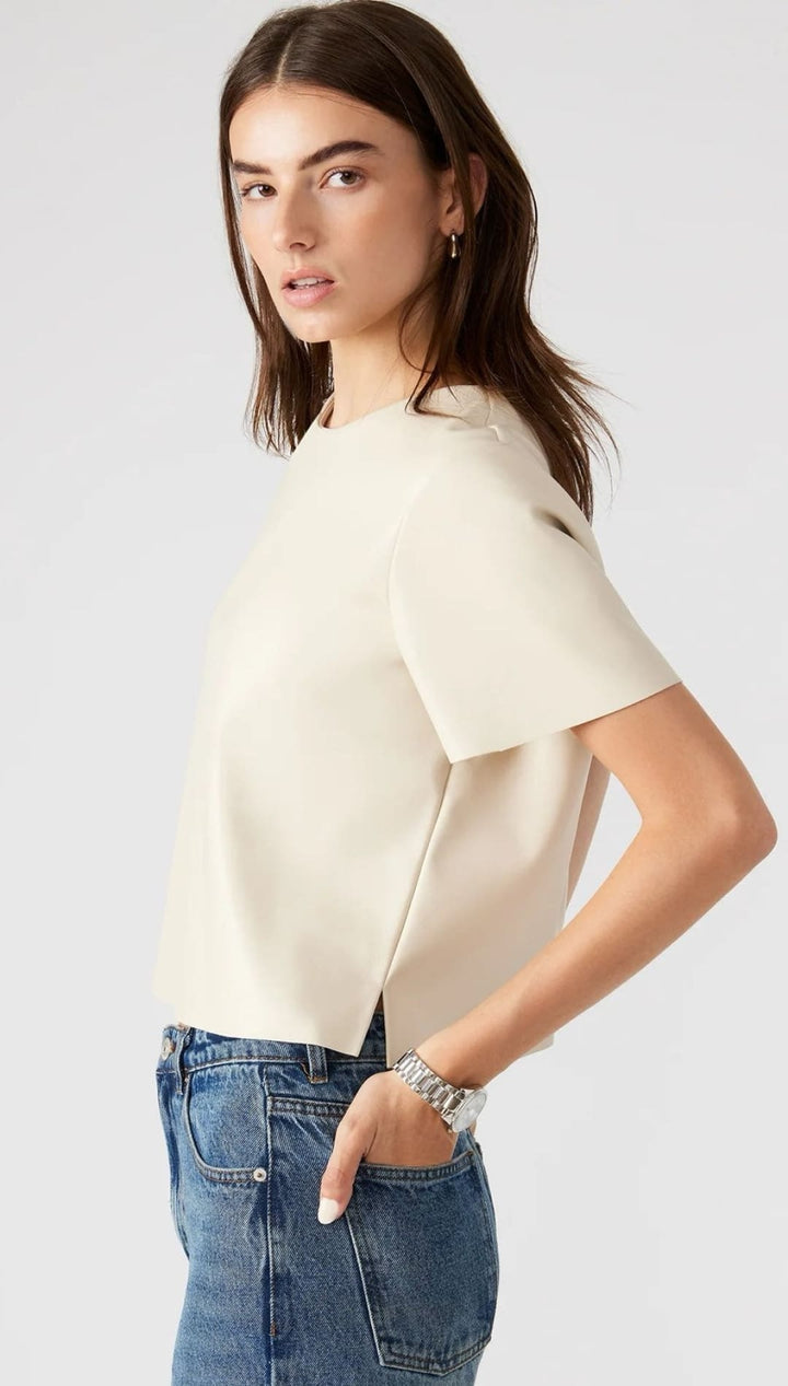 A woman wearing a light-colored short-sleeved top and blue jeans, with a silver watch on her left wrist.