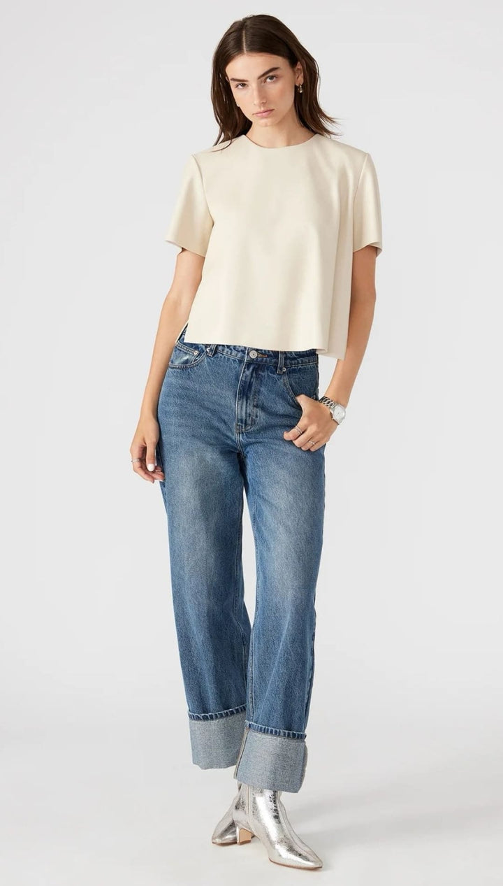 A woman models a casual outfit consisting of a cream-colored short-sleeved top, cuffed blue jeans, and silver pointed-toe boots.