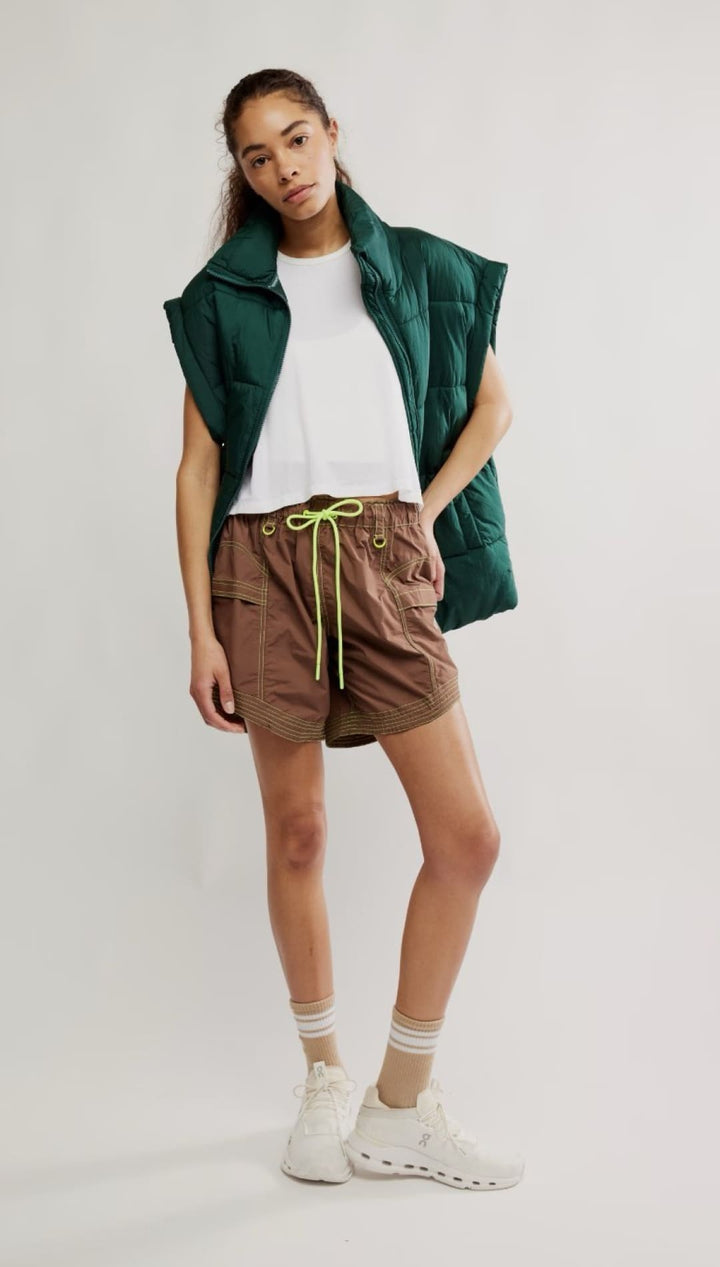 Woman’s outfit with green vest and brown shorts.