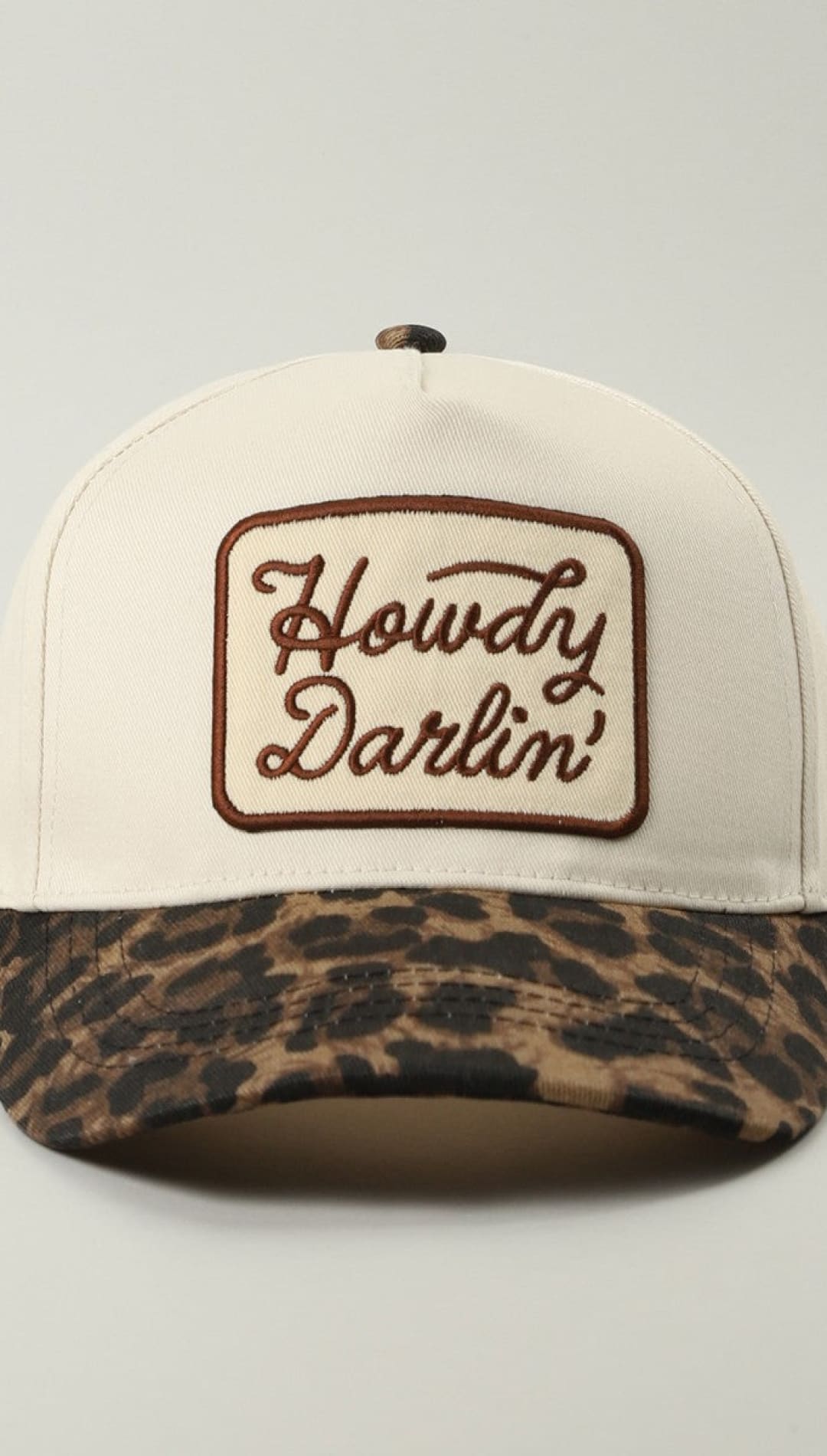 Leopard print baseball cap with ’howdy darlin’’ embroidery in brown on white background.