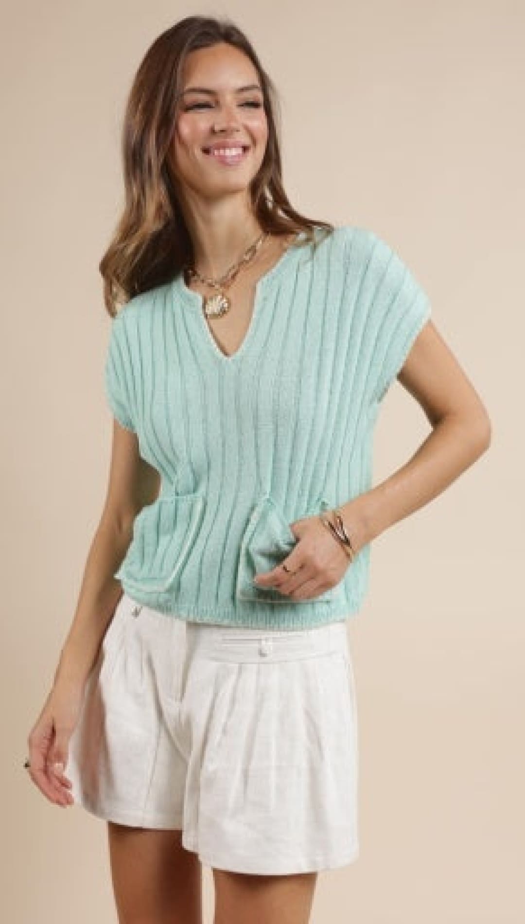Woman in a light green ribbed knit top and white shorts.