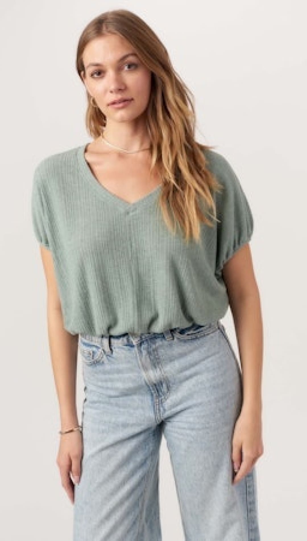 Woman’s sage green V-neck top with light blue jeans.