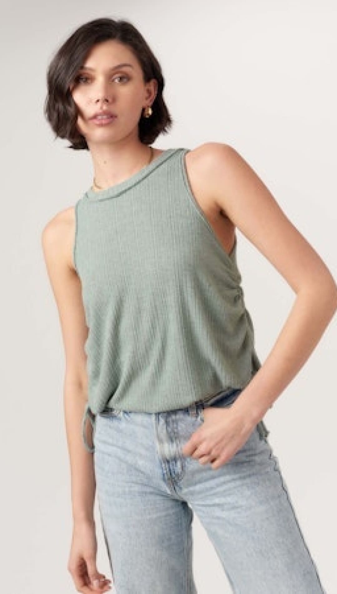 Woman wearing a ribbed, sleeveless, light green top and light blue jeans.