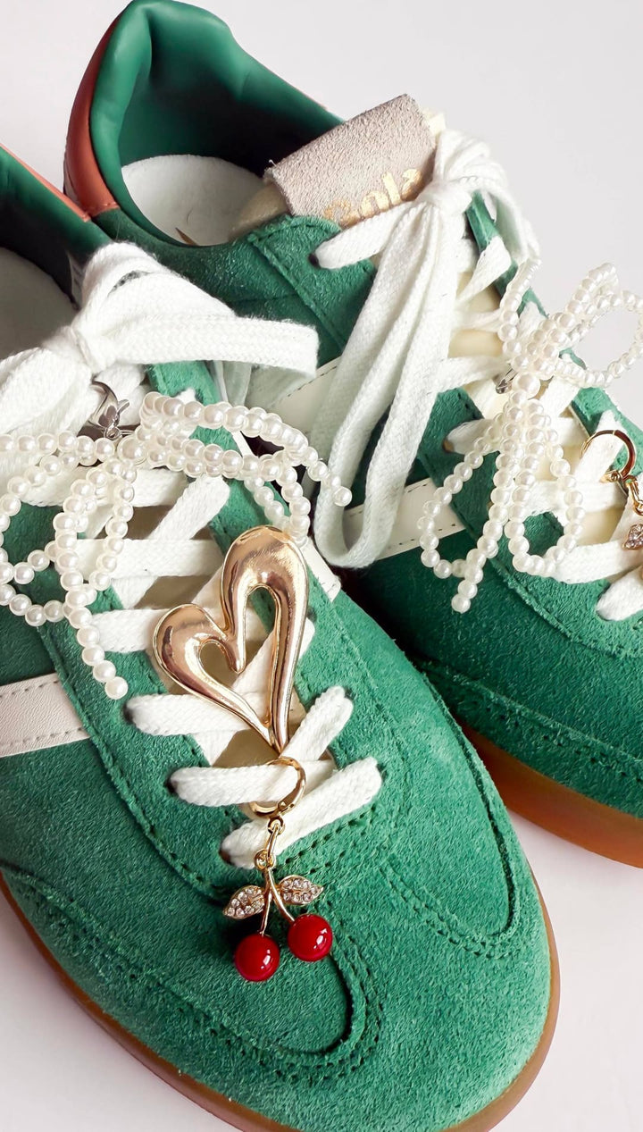Green suede sneakers with white laces and cherry charms.
