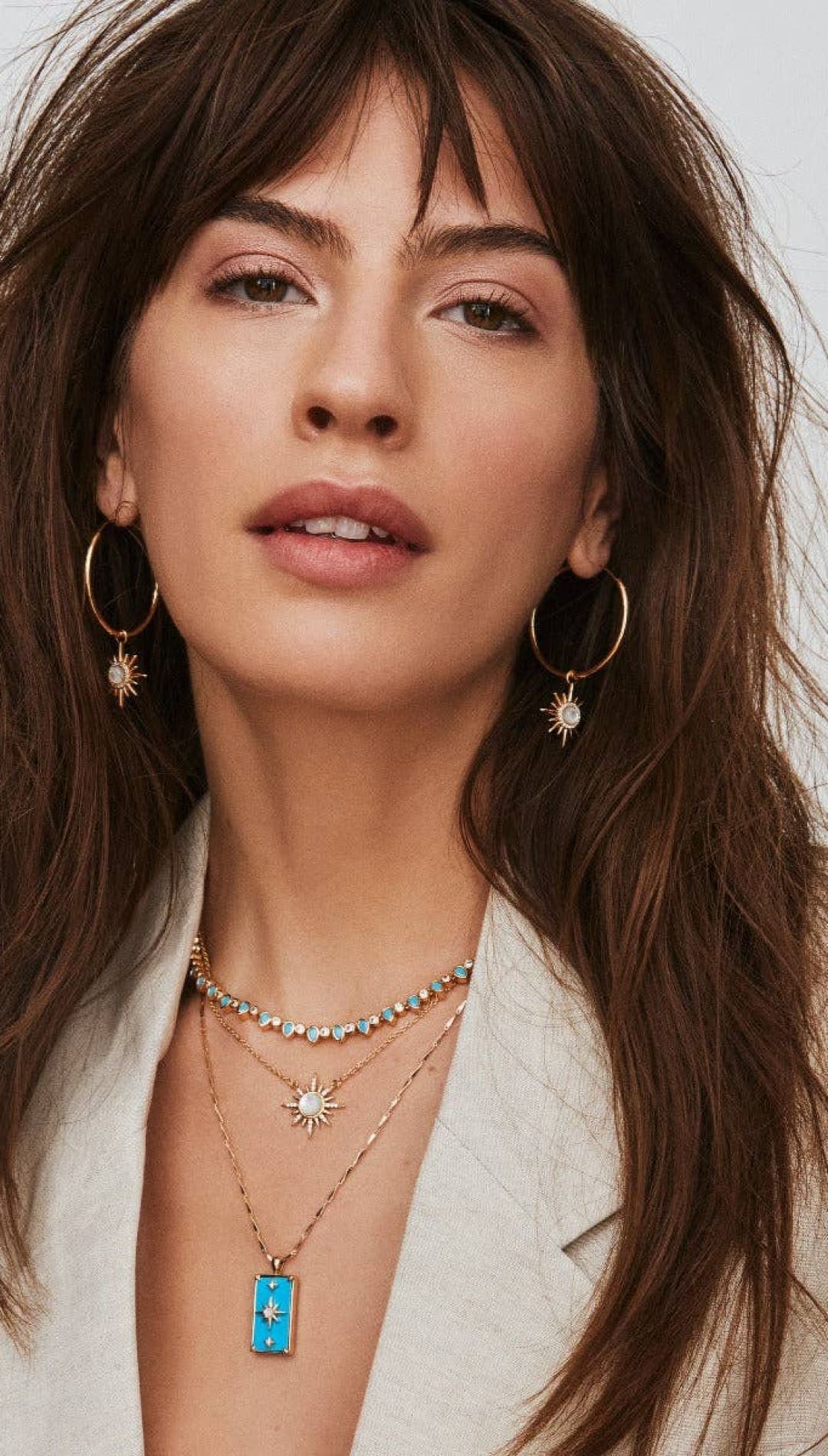 Woman wearing layered necklaces and hoop earrings.