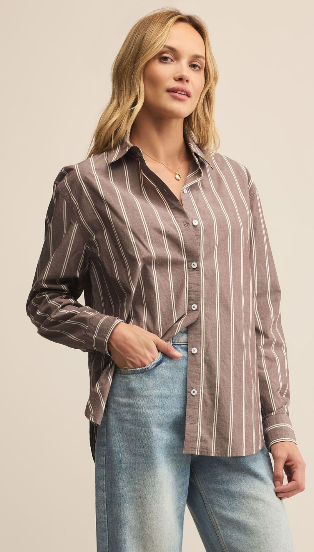 A woman wearing a brown and white striped button-down shirt and light blue jeans.