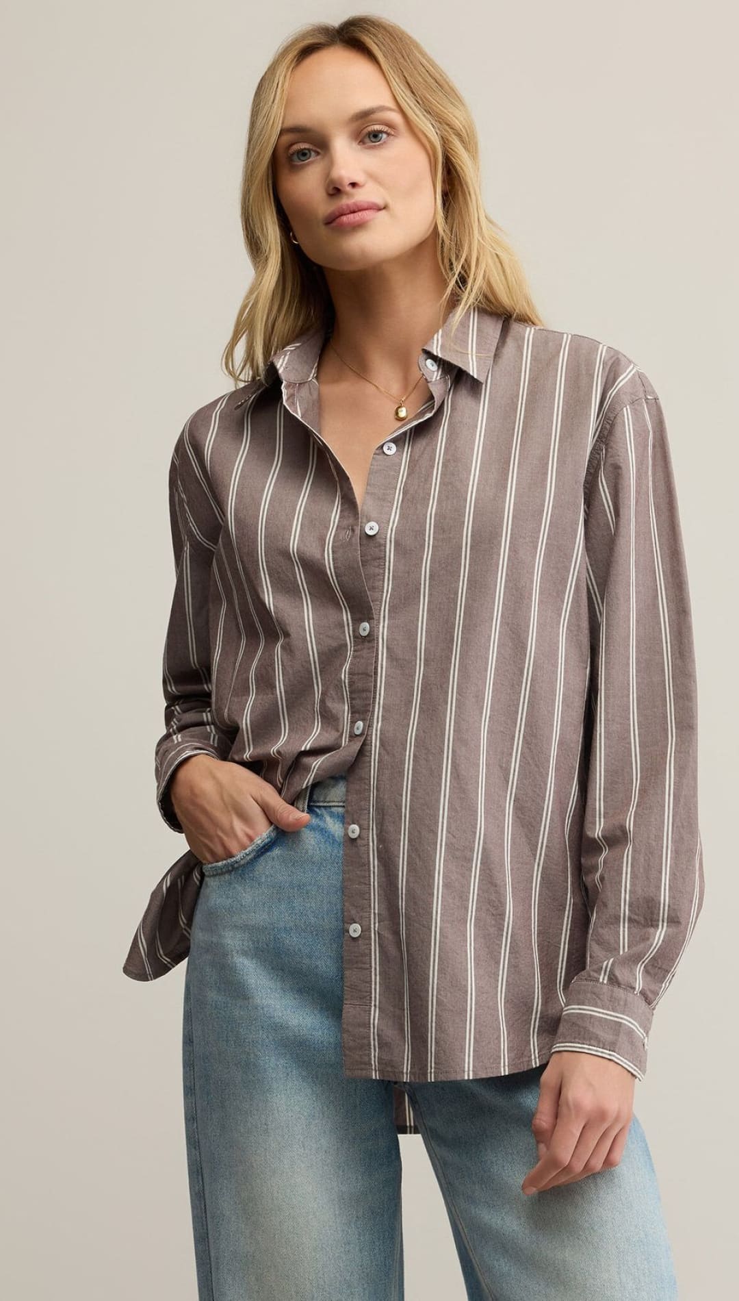 Women’s long-sleeved striped button-up shirt in a neutral tone paired with light wash denim jeans.