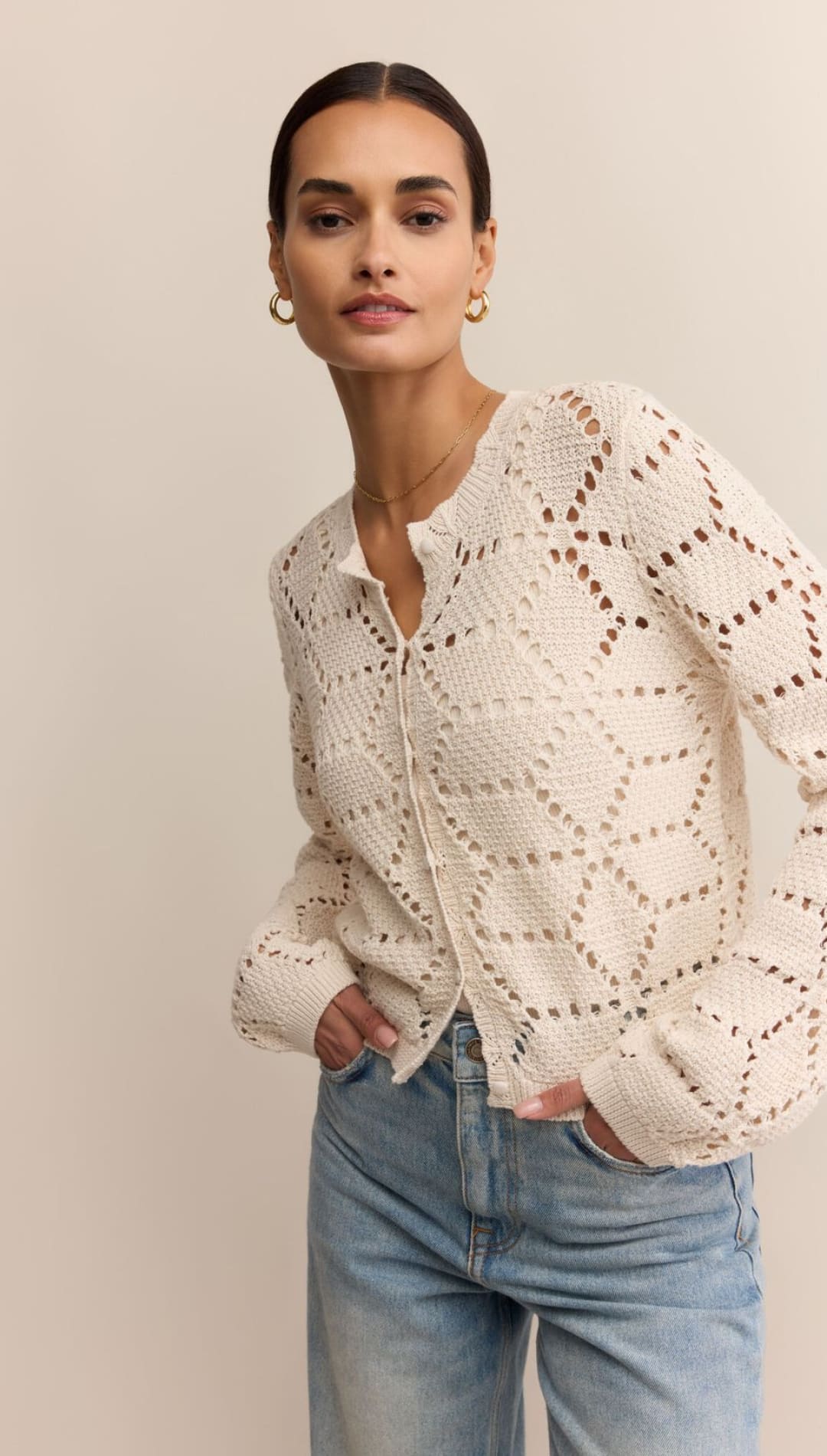 A woman models a long-sleeve, off-white, collared, open-knit cardigan with button closures.