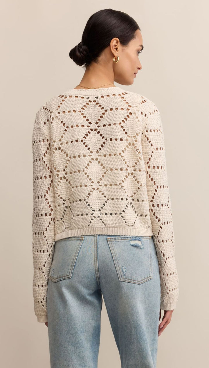 Women’s cream open-knit cardigan with light wash jeans.