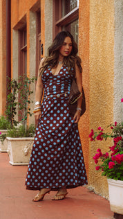 Woman in a long polka dot dress standing in front of a building with plants and flowers.