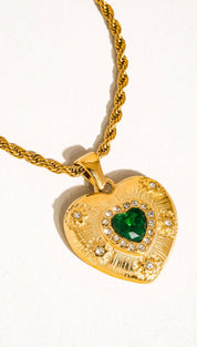 Gold heart-shaped pendant necklace with a central green gemstone surrounded by clear crystals and intricate engraved detailing.