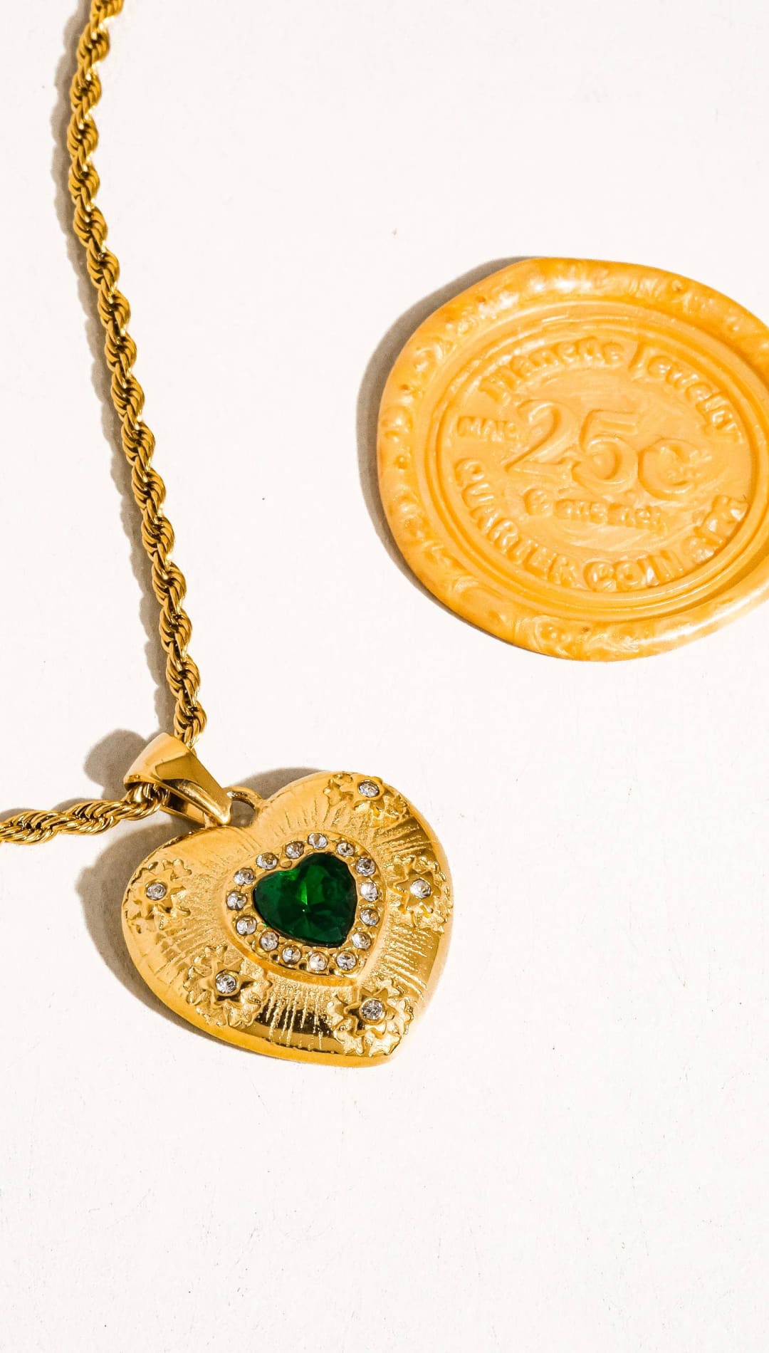 Gold heart-shaped pendant with a green gemstone and diamond accents, hanging from a gold rope chain.