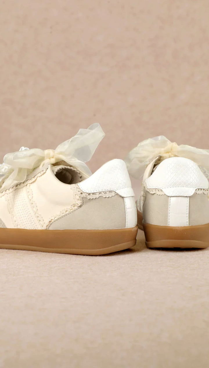 White lace-up sneakers with gold accents and bows, possibly by anthropologie.
