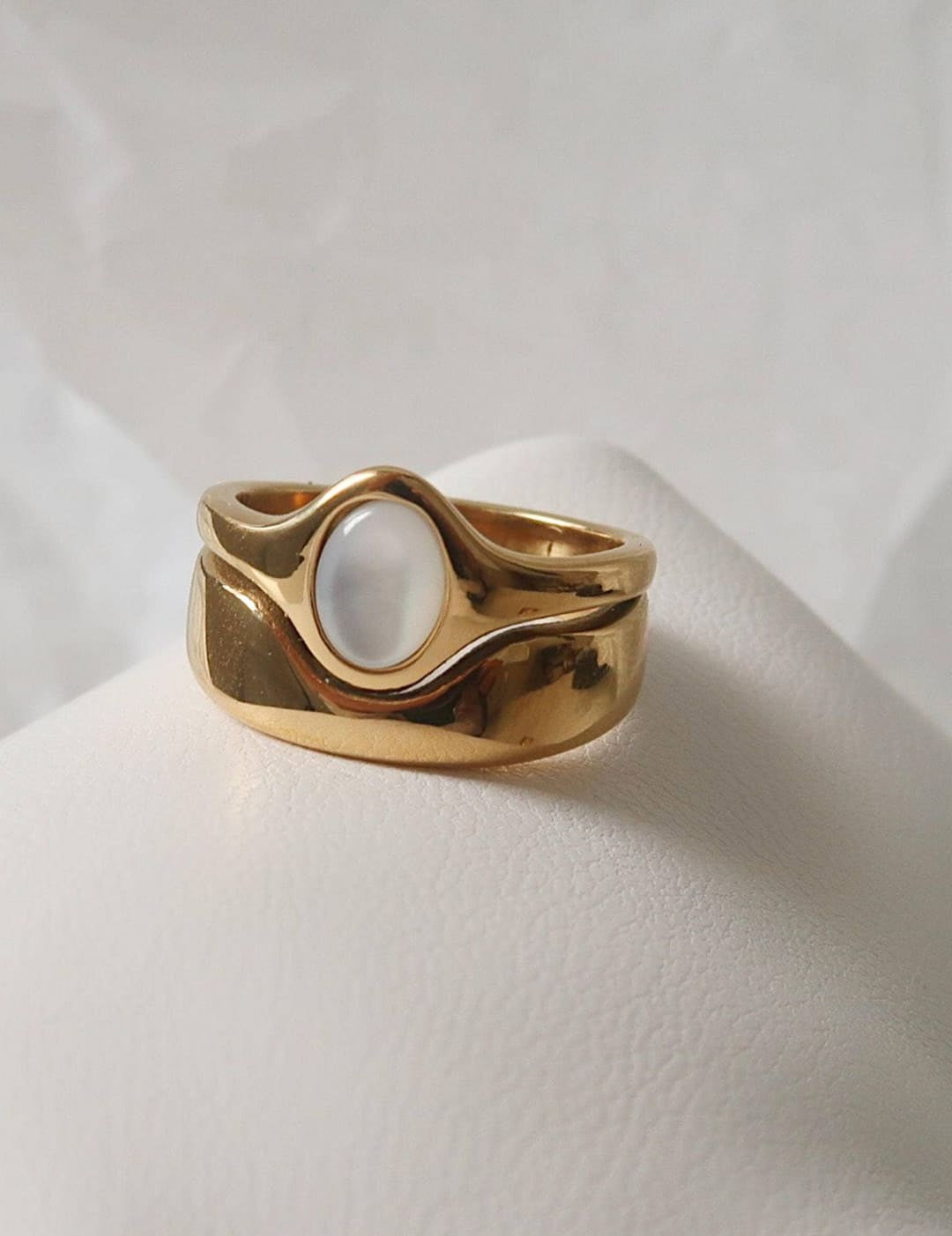 Gold-toned ring with a smooth, oval moonstone set in an organic, wavy band design.