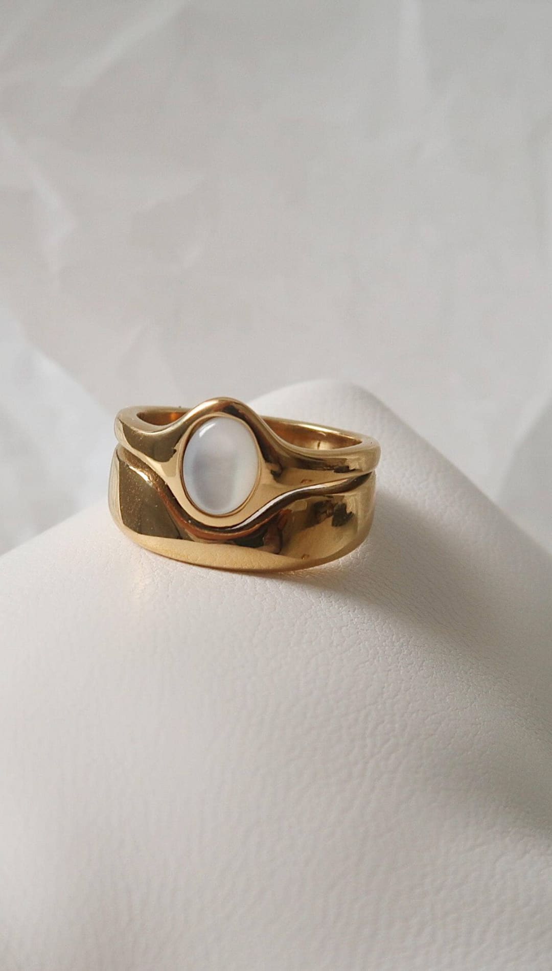Gold-toned ring with a smooth, oval moonstone set in an organic, wavy band design.
