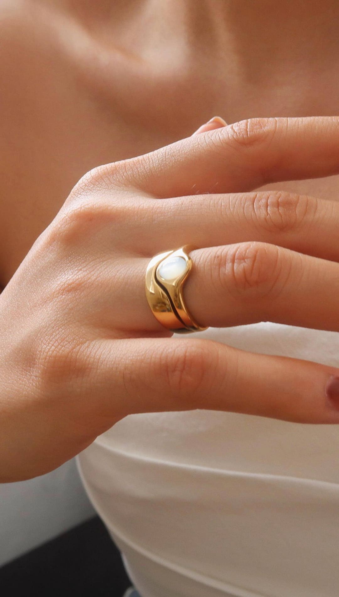 Gold ring with a smooth, wavy band and an embedded white opal stone.