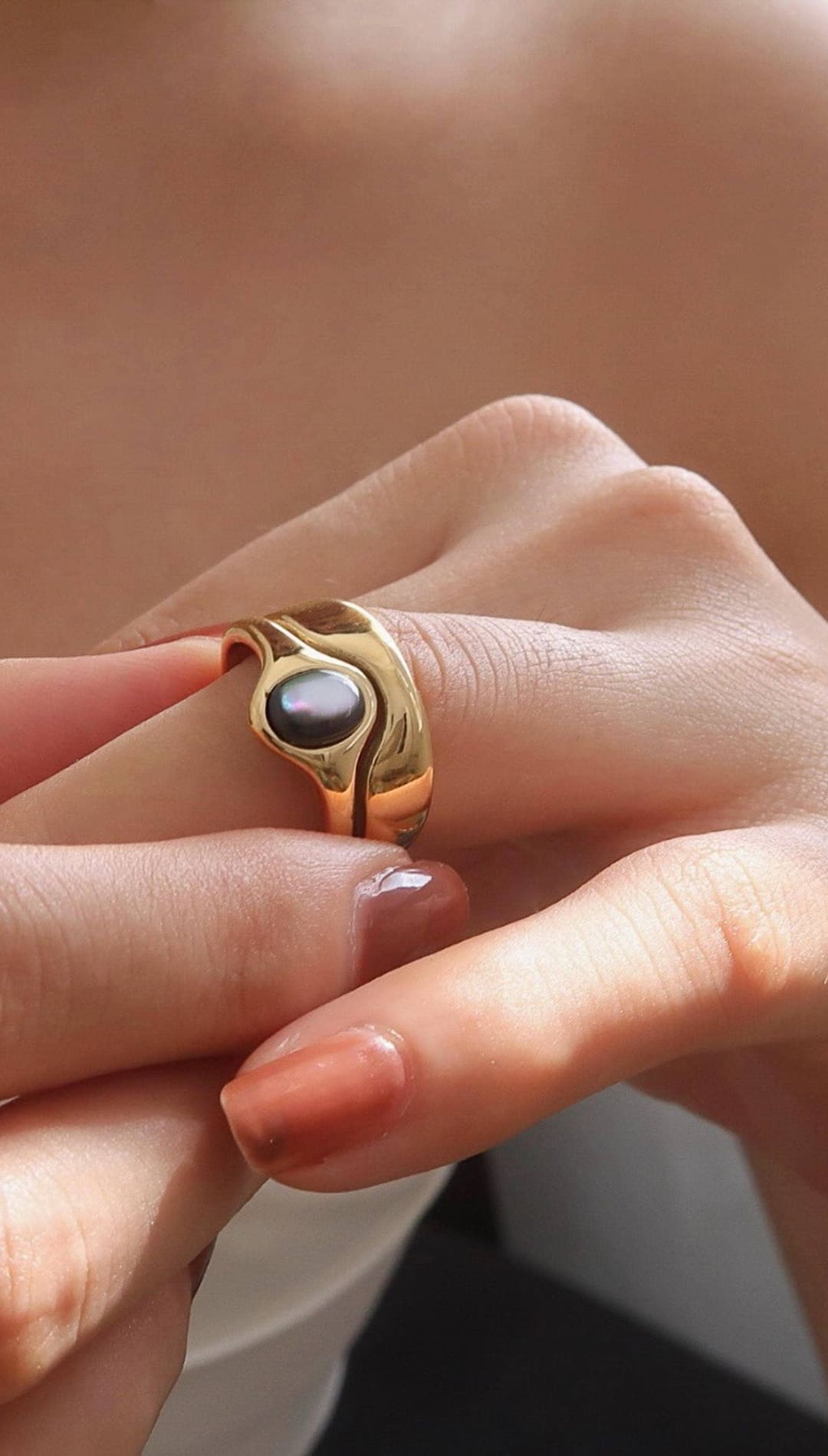 Gold-toned ring with a dark, iridescent pearl set in an organic, flowing design.