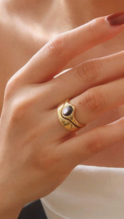 Gold-toned ring with a dark, oval-shaped stone set in an organic, sculptural band.
