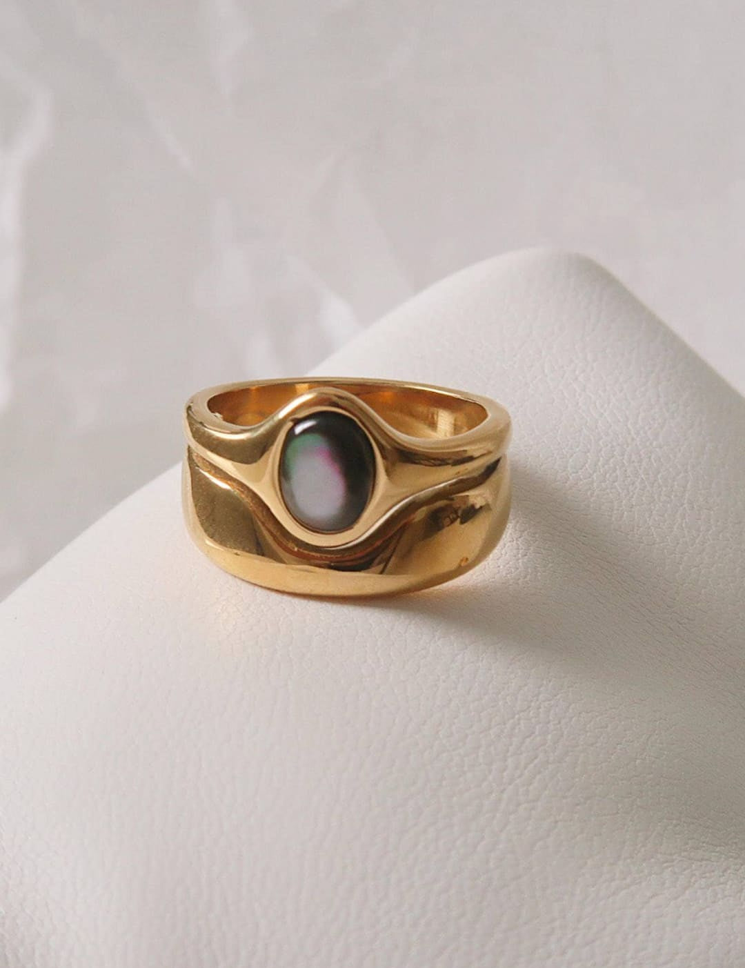 Gold-toned ring with a smooth, wavy band and an oval-shaped black mother-of-pearl centerpiece.