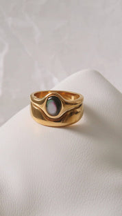 Gold-toned ring with a smooth, wavy band and an oval-shaped black mother-of-pearl centerpiece.