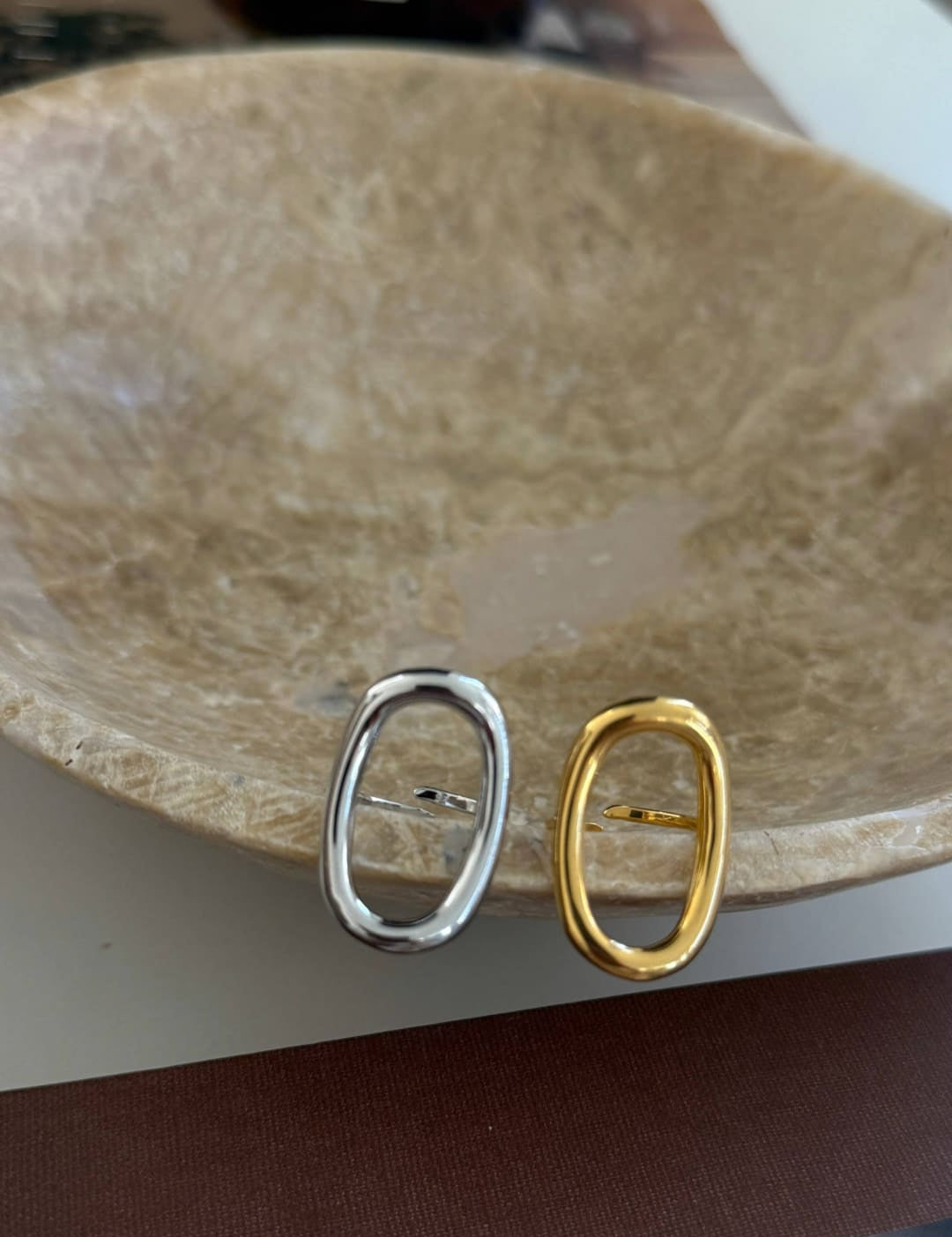 A pair of minimalist oval-shaped metal pin clasps, one in polished silver and the other in warm gold tone.