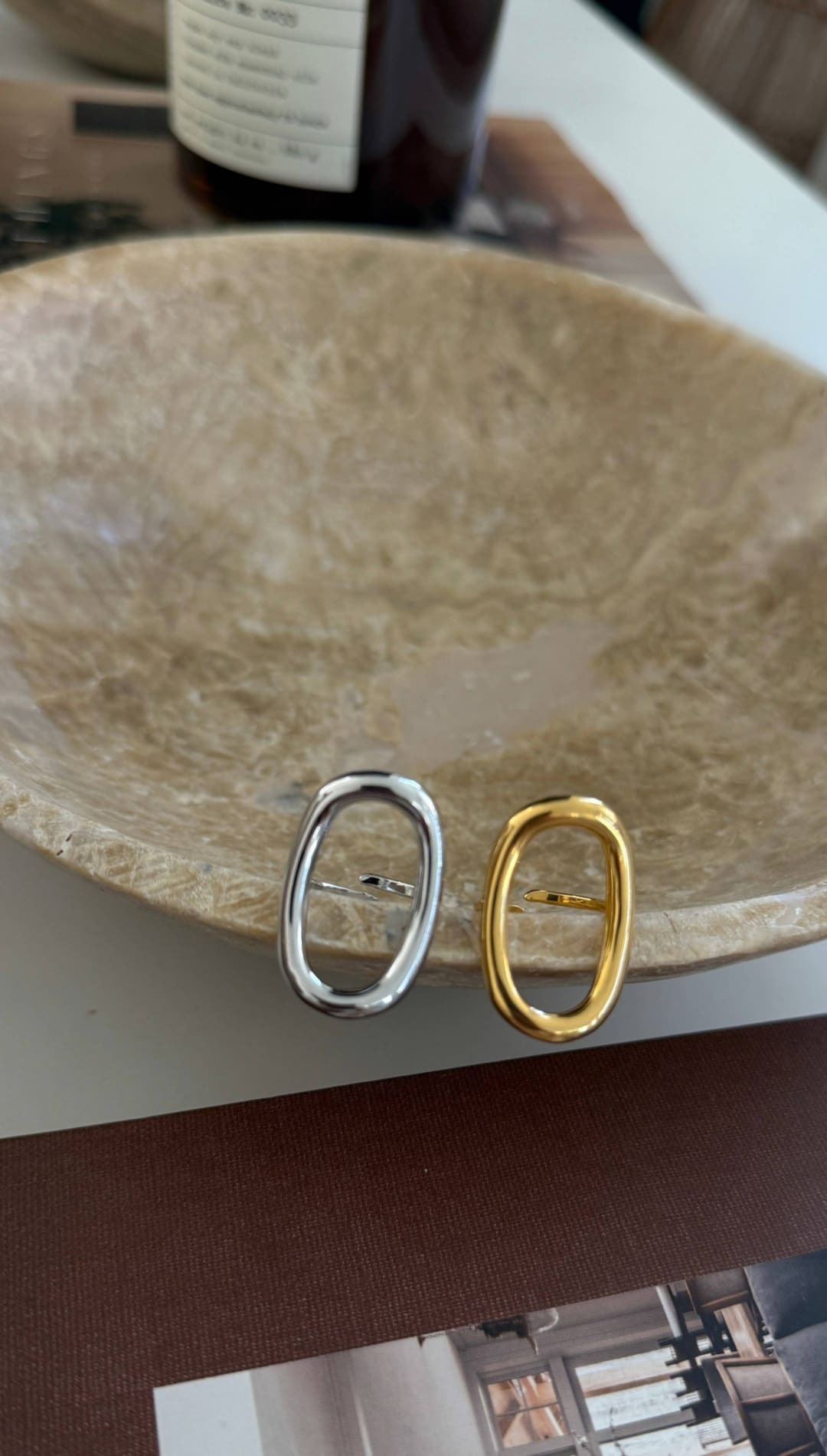 A pair of minimalist oval-shaped metal pin clasps, one in polished silver and the other in warm gold tone.