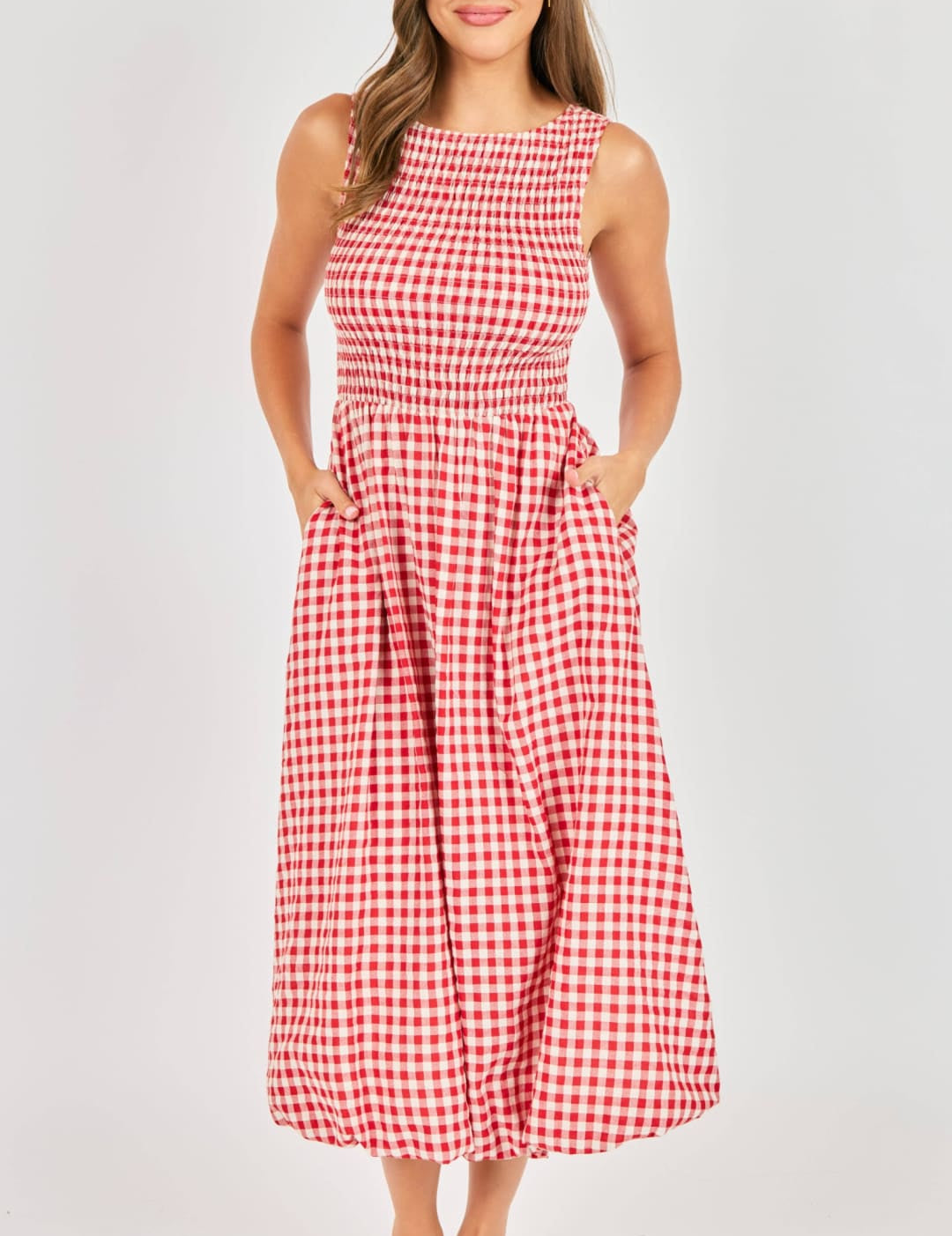 A red and white gingham sleeveless midi dress with a fitted bodice, smocked waistband, and two side pockets.