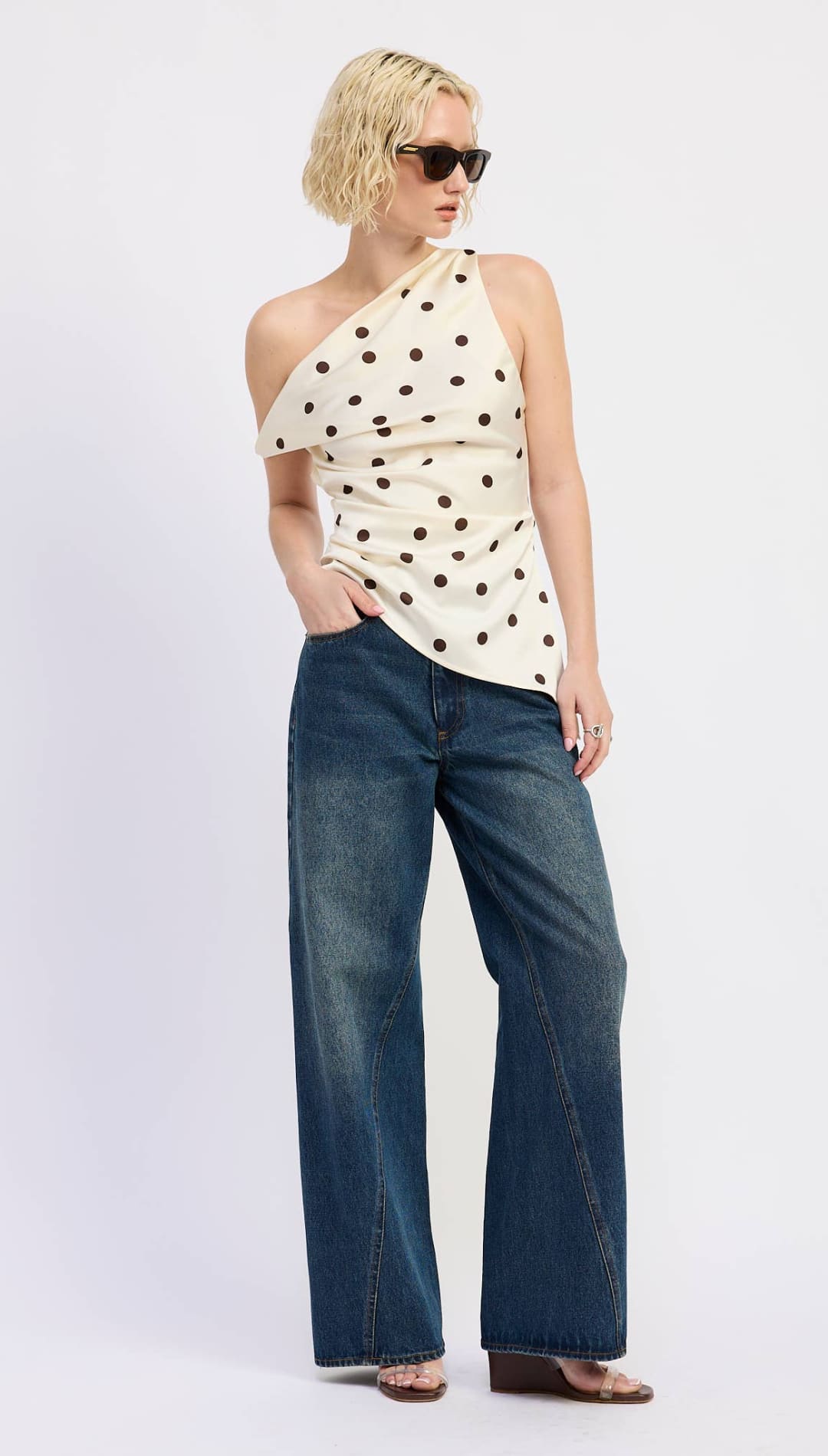 A cream-colored one-shoulder top with black polka dots, made of a soft, stretchy fabric.