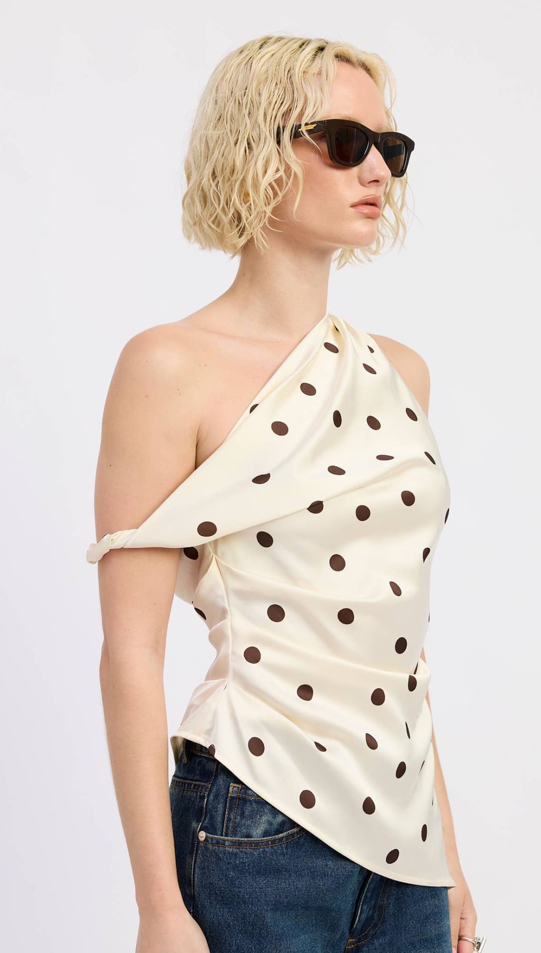 Cream-colored satin one-shoulder top with black polka dots and a twisted arm detail.