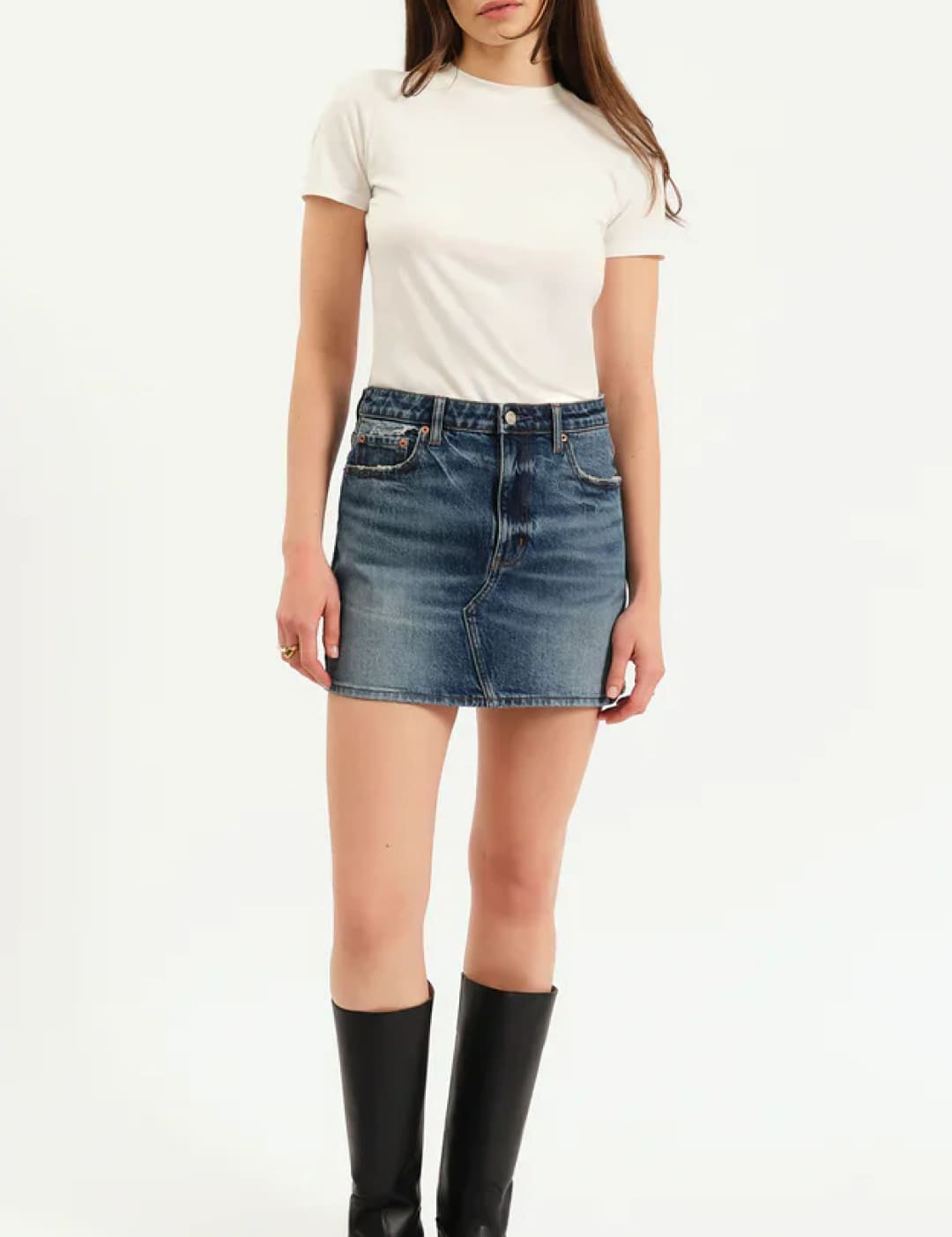 A woman wearing a white short-sleeve crewneck t-shirt, a blue denim mini skirt, and black knee-high boots.