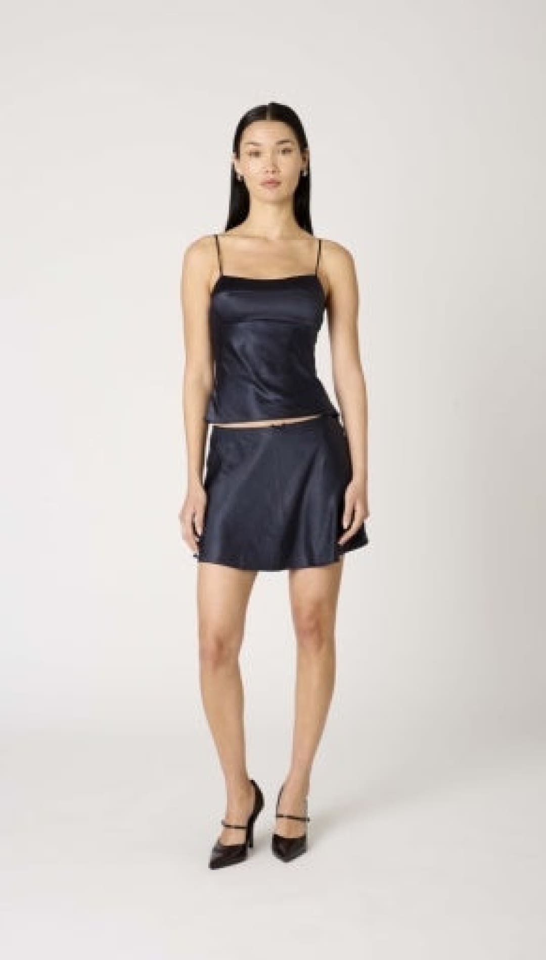 A woman wearing a dark blue satin camisole and matching mini skirt with black high heels.