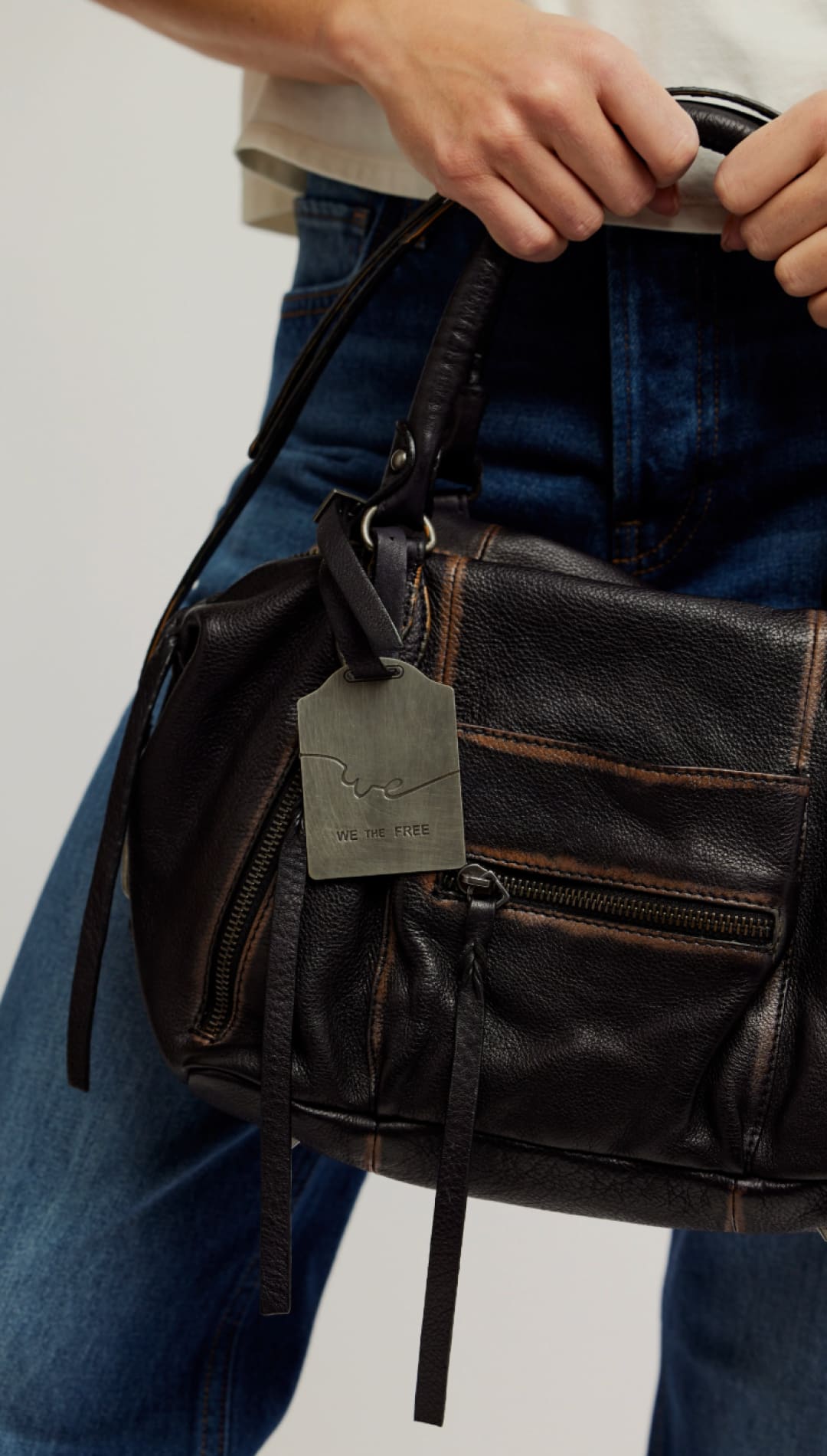 Dark brown leather handbag with visible stitching and a metal tag that reads ’we the free.’