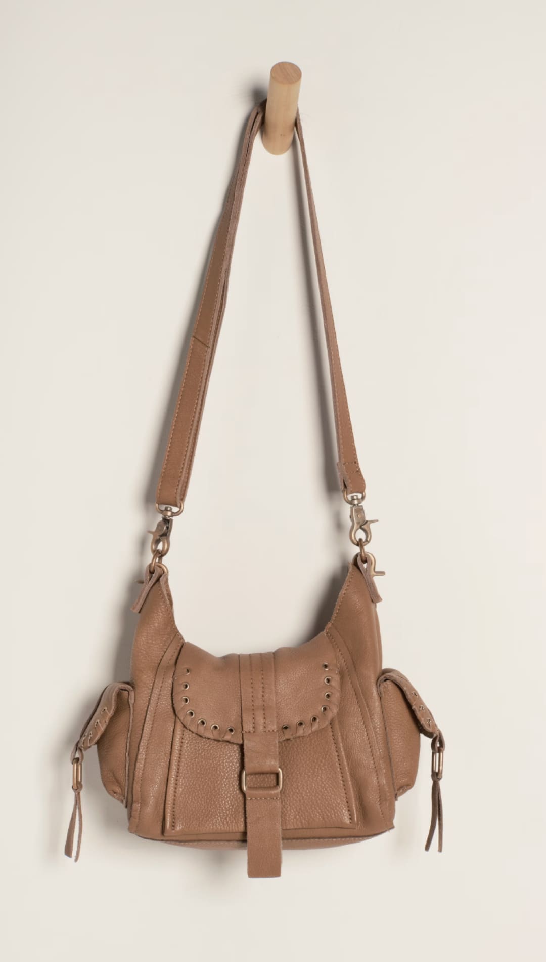 Tan leather crossbody bag with a flap closure, decorative stitching and tassels on the sides.
