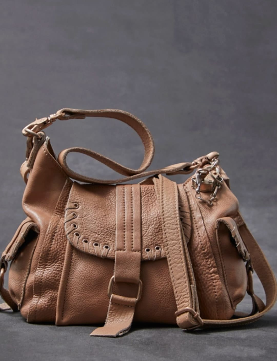 Tan leather crossbody bag with a textured surface, adjustable strap, and decorative metal hardware.