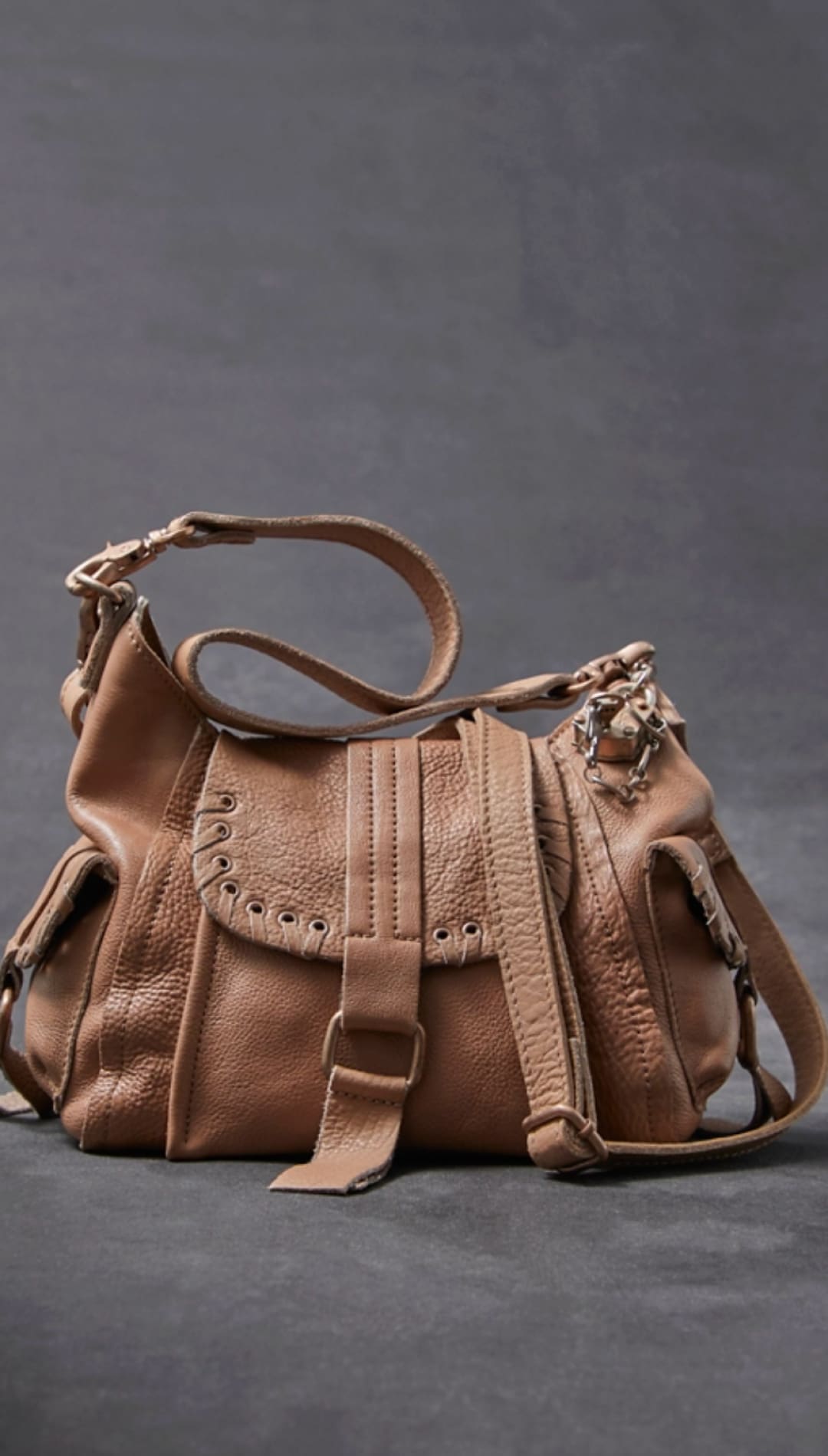 Tan leather crossbody bag with a textured surface, adjustable strap, and decorative metal hardware.