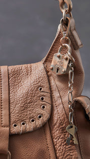 Tan leather handbag with a metallic padlock charm and keychain attached to the strap.