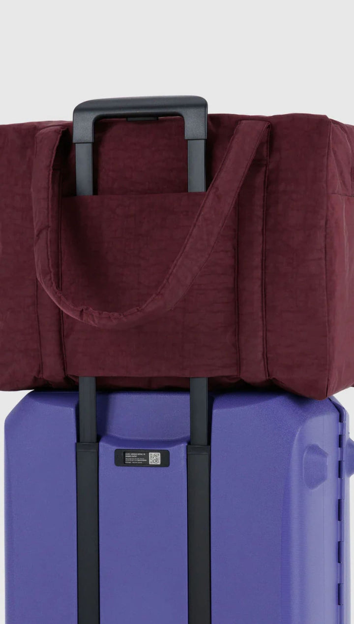 Maroon tote bag with black handles and trim, placed on top of a blue suitcase.