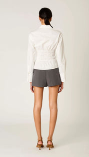 White long-sleeved blouse with a cinched waist and subtle pleating detail
