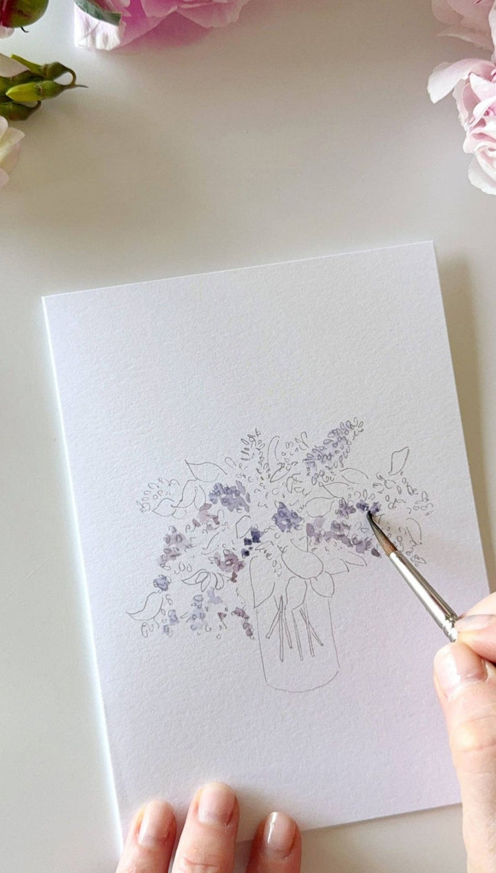 White floral sketchbook with silver pen and purple ink bottle.
