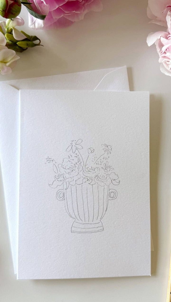 White vase sketchbook with floral design on cover, watercolor paint tube and brush nearby.
