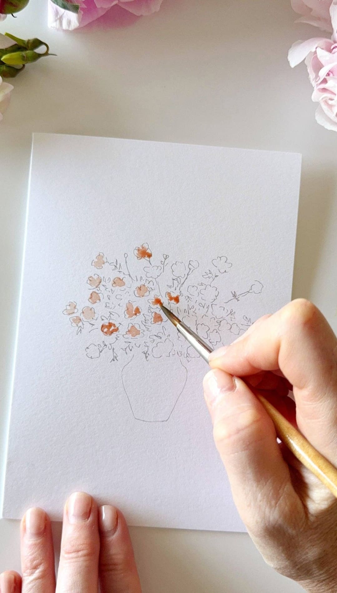 Wooden paintbrush with orange and white bristles, used for painting flowers in a vase illustration.