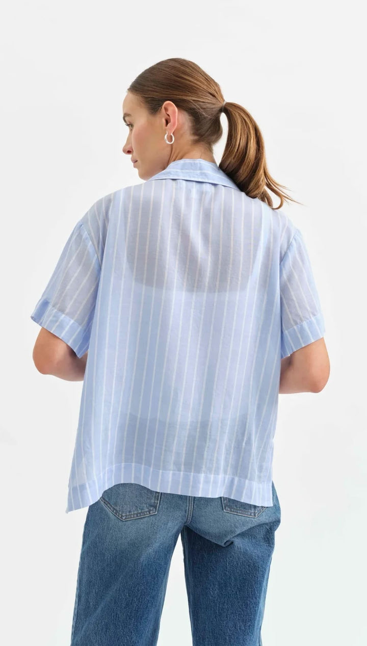 Light blue striped short-sleeve button-up shirt worn with blue jeans.