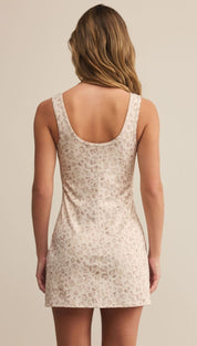 A woman wearing a sleeveless, scoop-neck, light-colored mini dress with a subtle animal print.