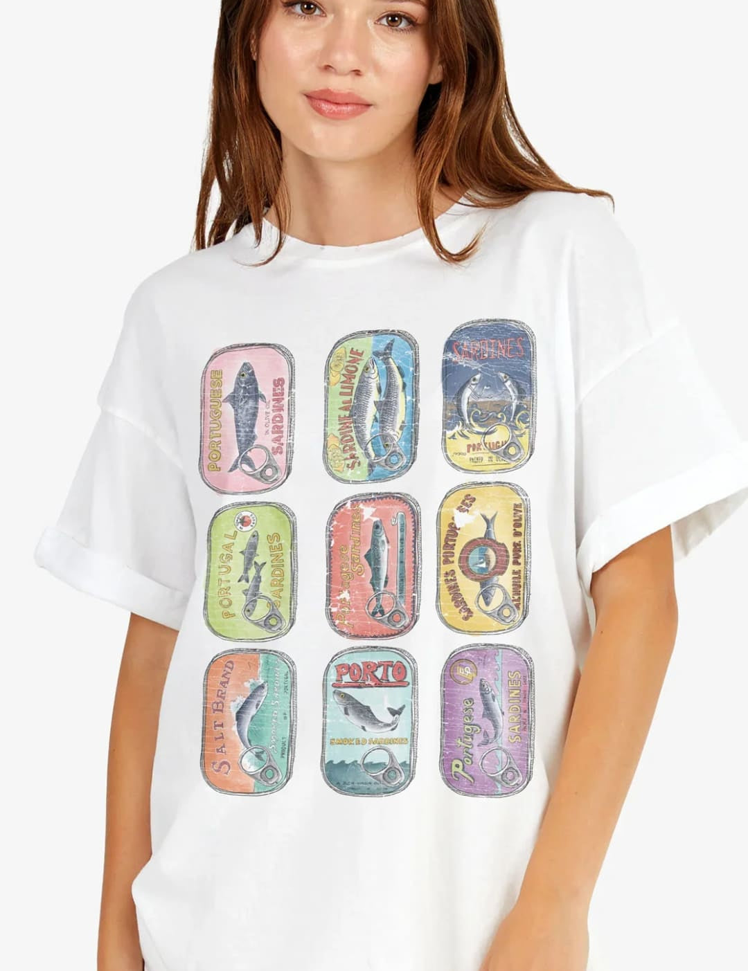 White oversized t-shirt featuring a vibrant, vintage-style graphic of nine colorful canned fish labels arranged in a grid.