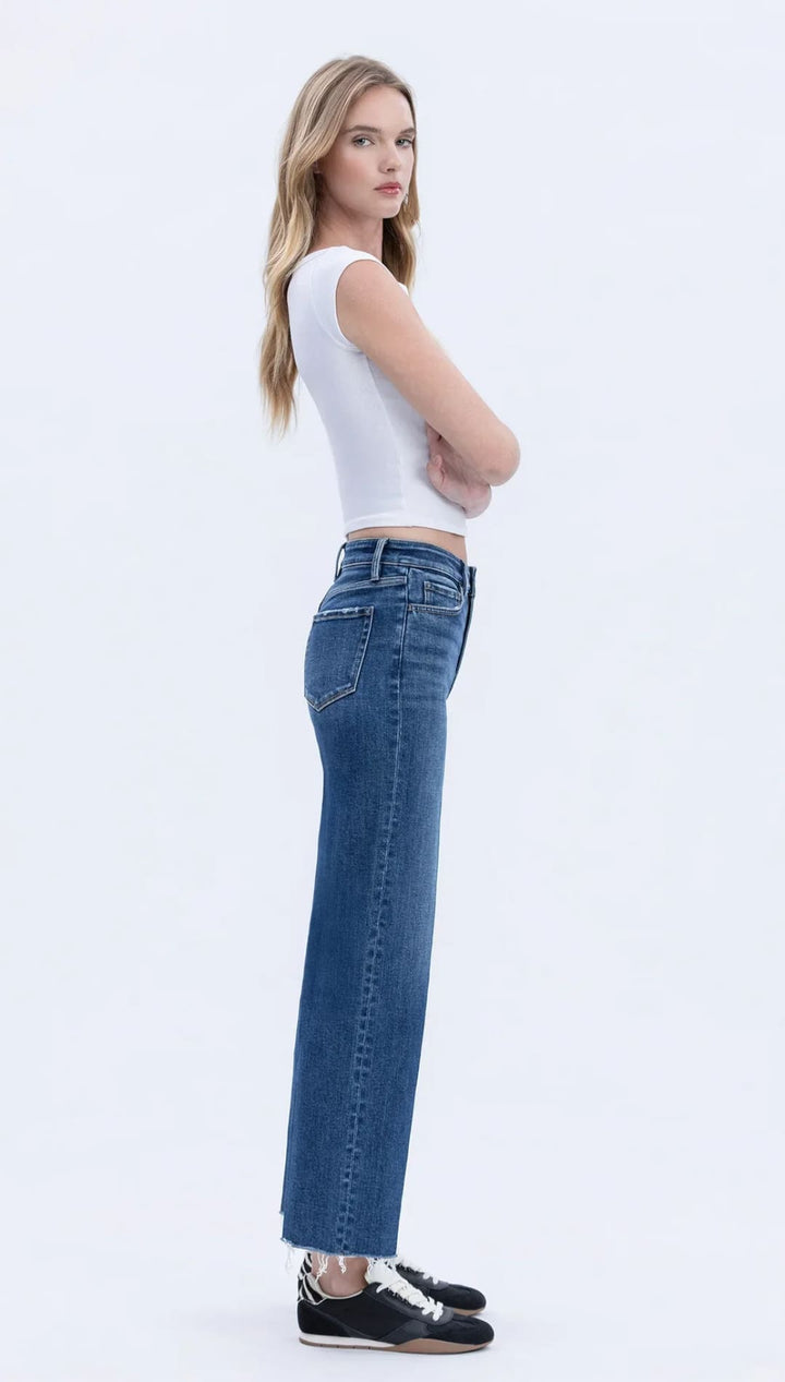 Woman wearing a white sleeveless top, blue wide-leg jeans, and black sneakers.