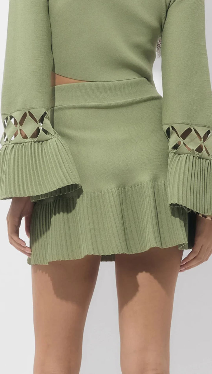 Olive green pleated mini skirt with cutout details and ruffled hem, likely made of stretchy fabric.